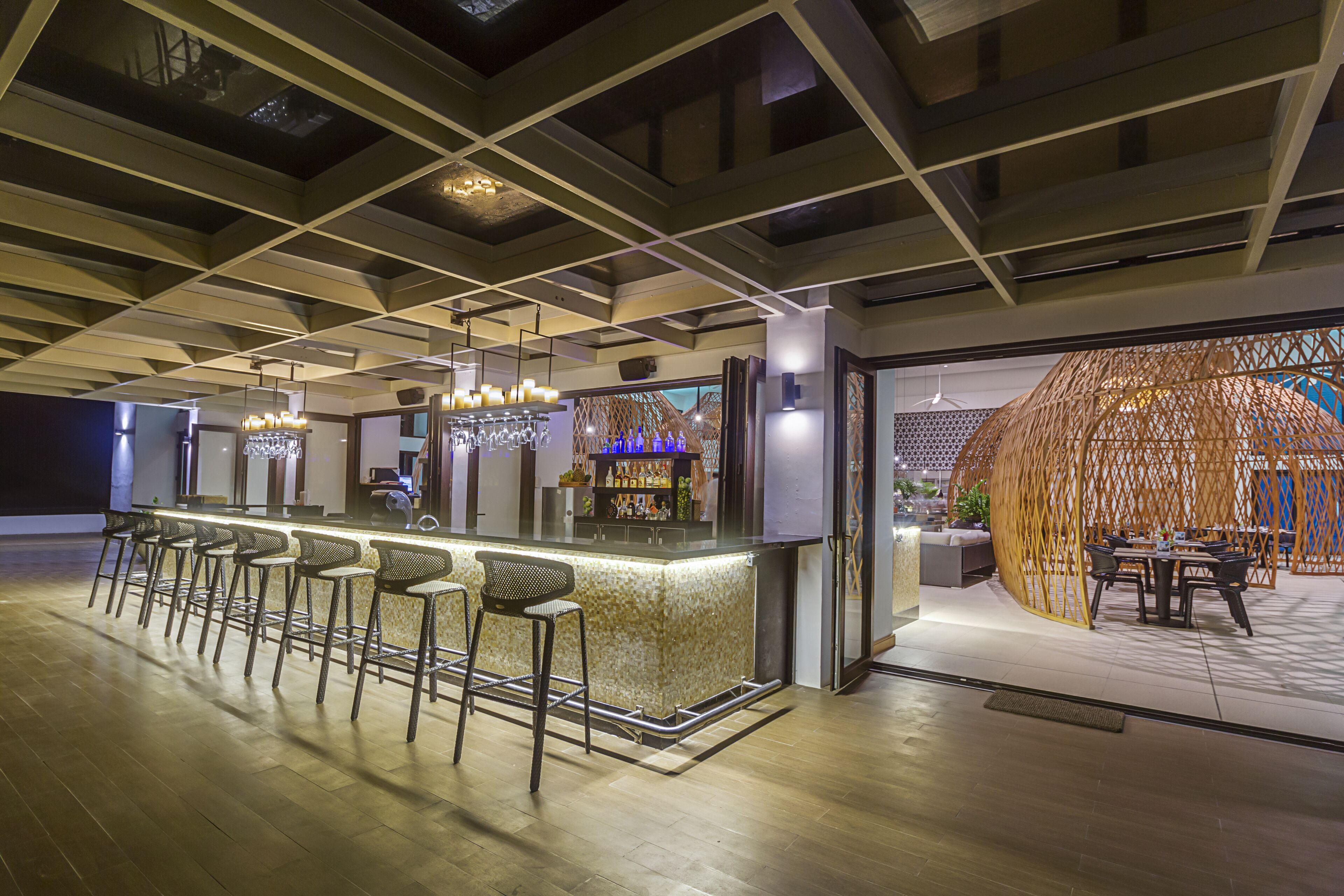Un espace bar moderne doté d’un long comptoir, de nombreux tabourets et d’un coin salon avec des tables et des chaises.