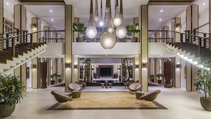 Een ruime lobby met een centrale zithoek, een trap en hangende lampen.