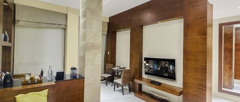 Quarto de hotel moderno com área de estar, espaço para refeições e televisão na parede.