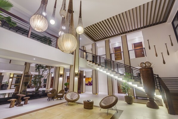 A spacious lobby with a staircase, hanging lights, and comfortable seating areas.
