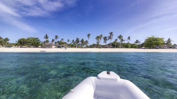 A boat on clear turquoise water with a beach and palm trees in the background.