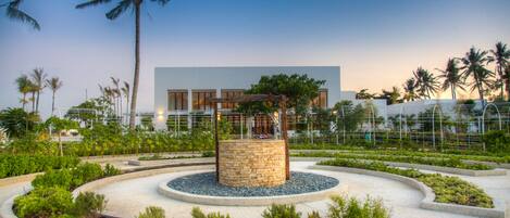 A landscaped garden with a central stone structure, palm trees, and a modern building in the background.