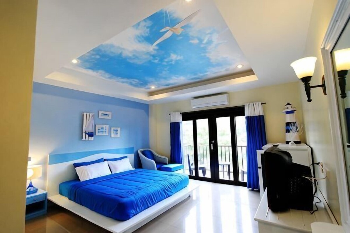 A bedroom with a bed, a chair, a desk, and a ceiling mural.