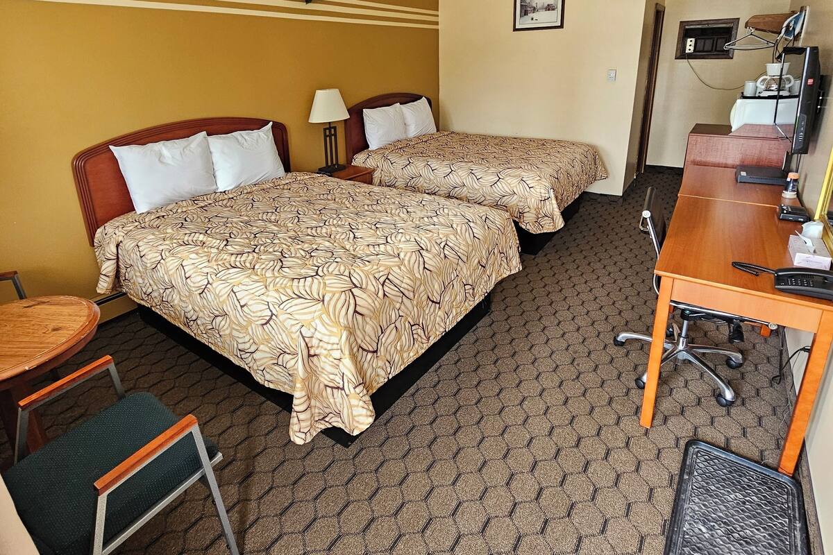 Une chambre d’hôtel avec deux lits, un bureau, une chaise, une petite table et un téléviseur.