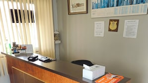 A reception desk with a check-out counter, a calendar, a small decorative item, and a framed picture on the wall. - Forest Plaza Motel (Wellington North)