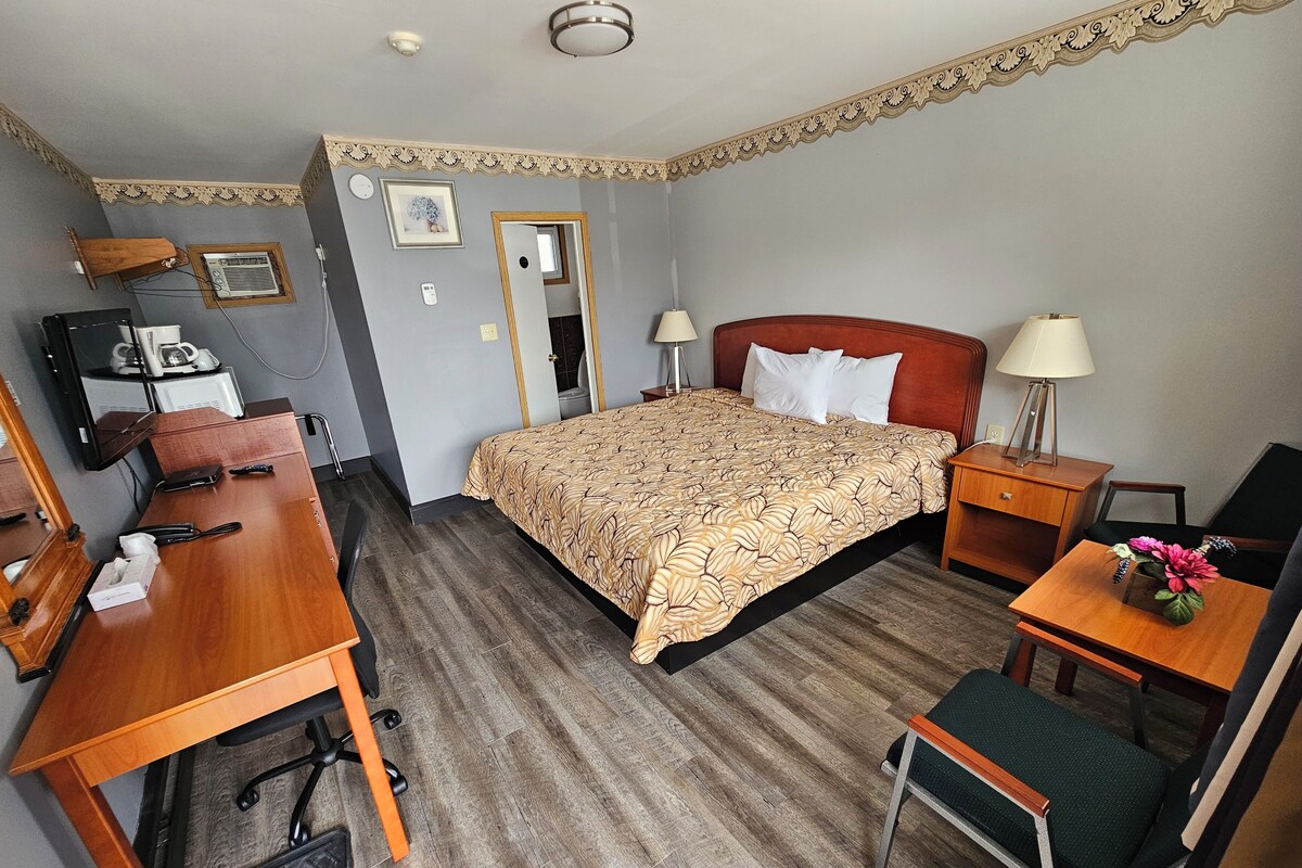 Una habitación de hotel con cama, escritorio, silla y una pequeña mesa con lámpara y flores.