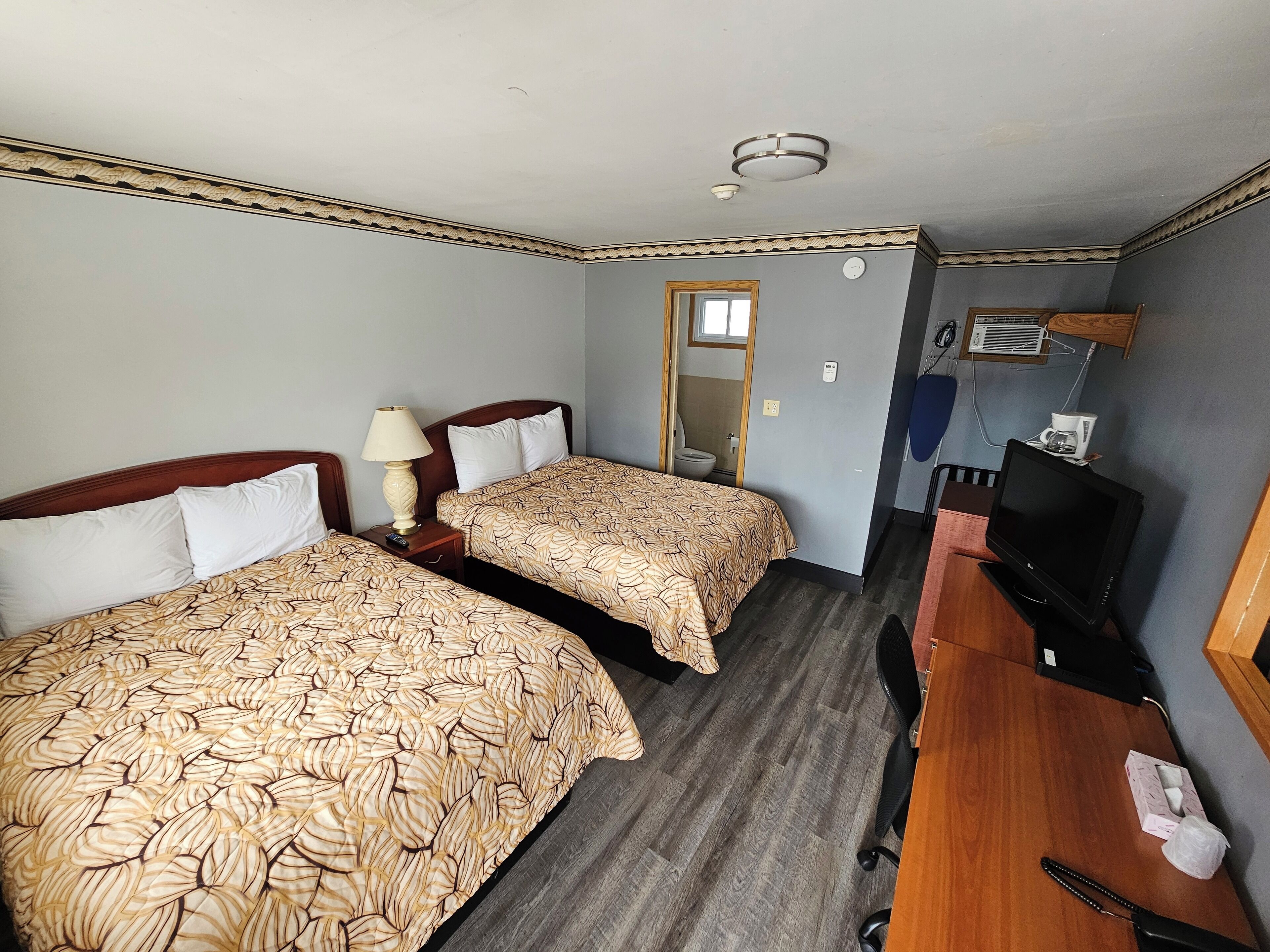 A hotel room with two beds, a desk with a TV, and a bathroom visible through a door.