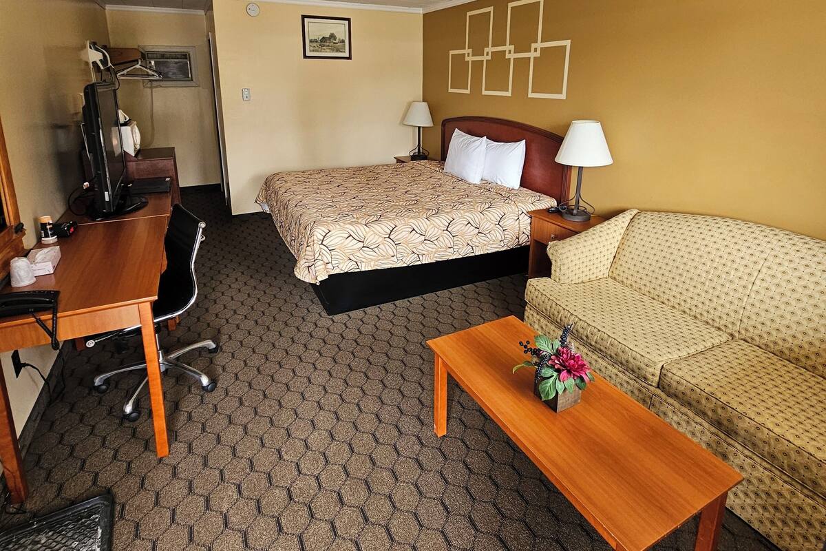 Une chambre d’hôtel comprenant un lit, un bureau, une chaise, un canapé et une petite table agrémentée d’un vase de fleurs.