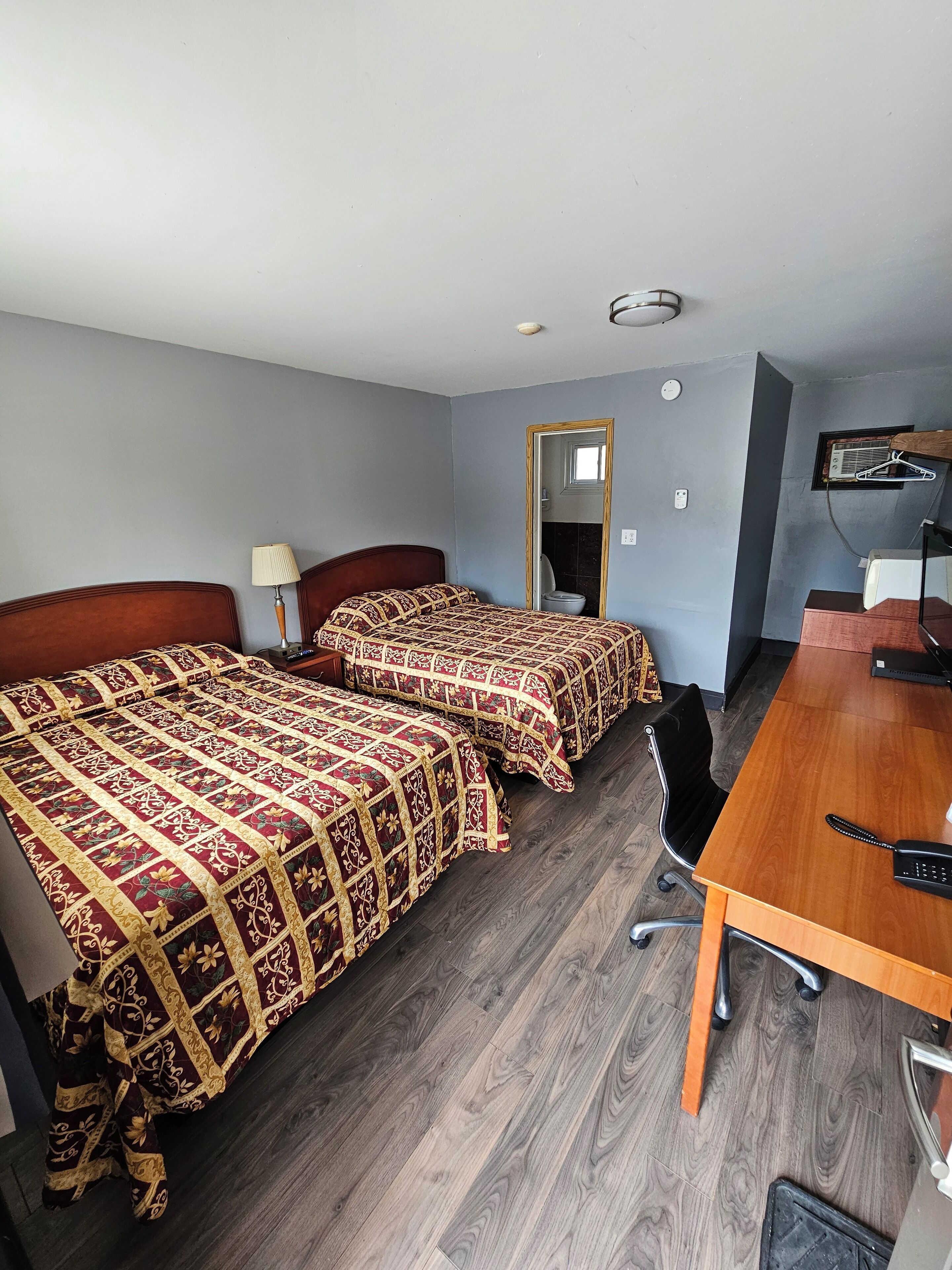 A room with two beds, a wooden desk, a chair, a lamp, and a mirror.