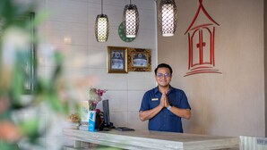 A hotel reception desk with a wooden counter, a name tag, a computer, and framed pictures on the wall. - Angkul Angkul Beach In Kuta (Kuta)