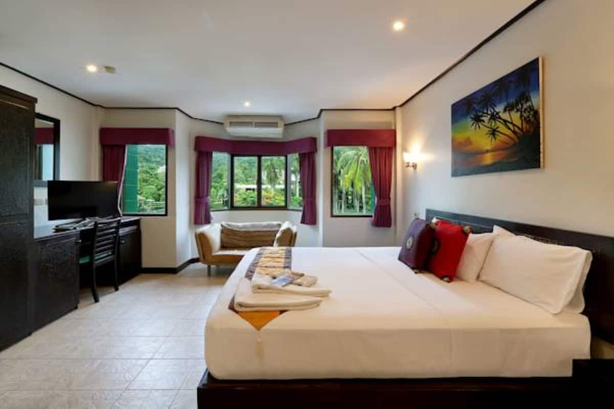 Habitación de hotel con una cama grande, un escritorio y una silla. Hay ventanas con cortinas, un cuadro en la pared y un televisor sobre el escritorio.