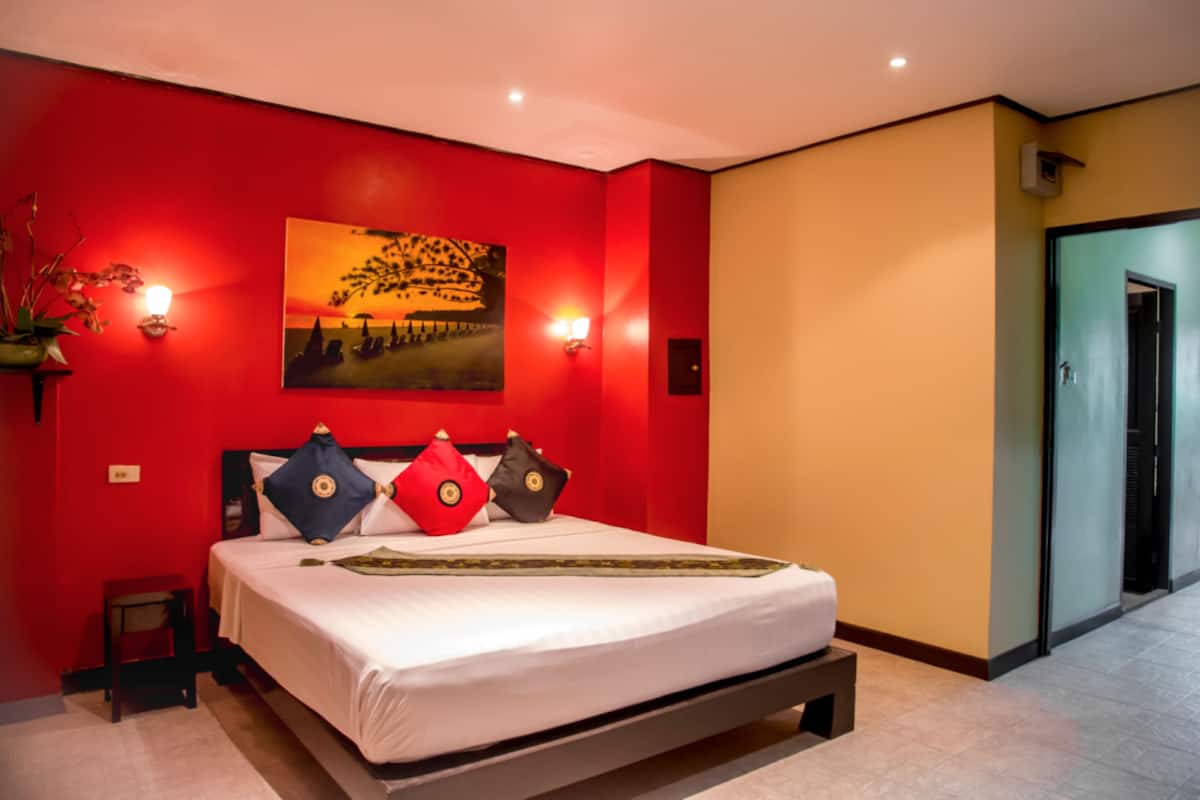 Un dormitorio con una cama, paredes rojas, un cuadro y apliques de pared.