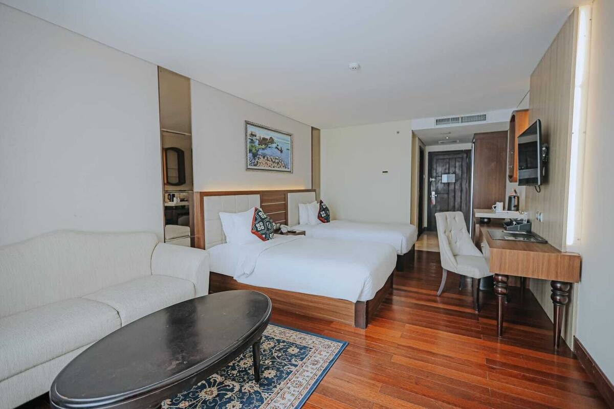 Habitación de hotel con sofá, dos camas, escritorio, silla y televisión.
