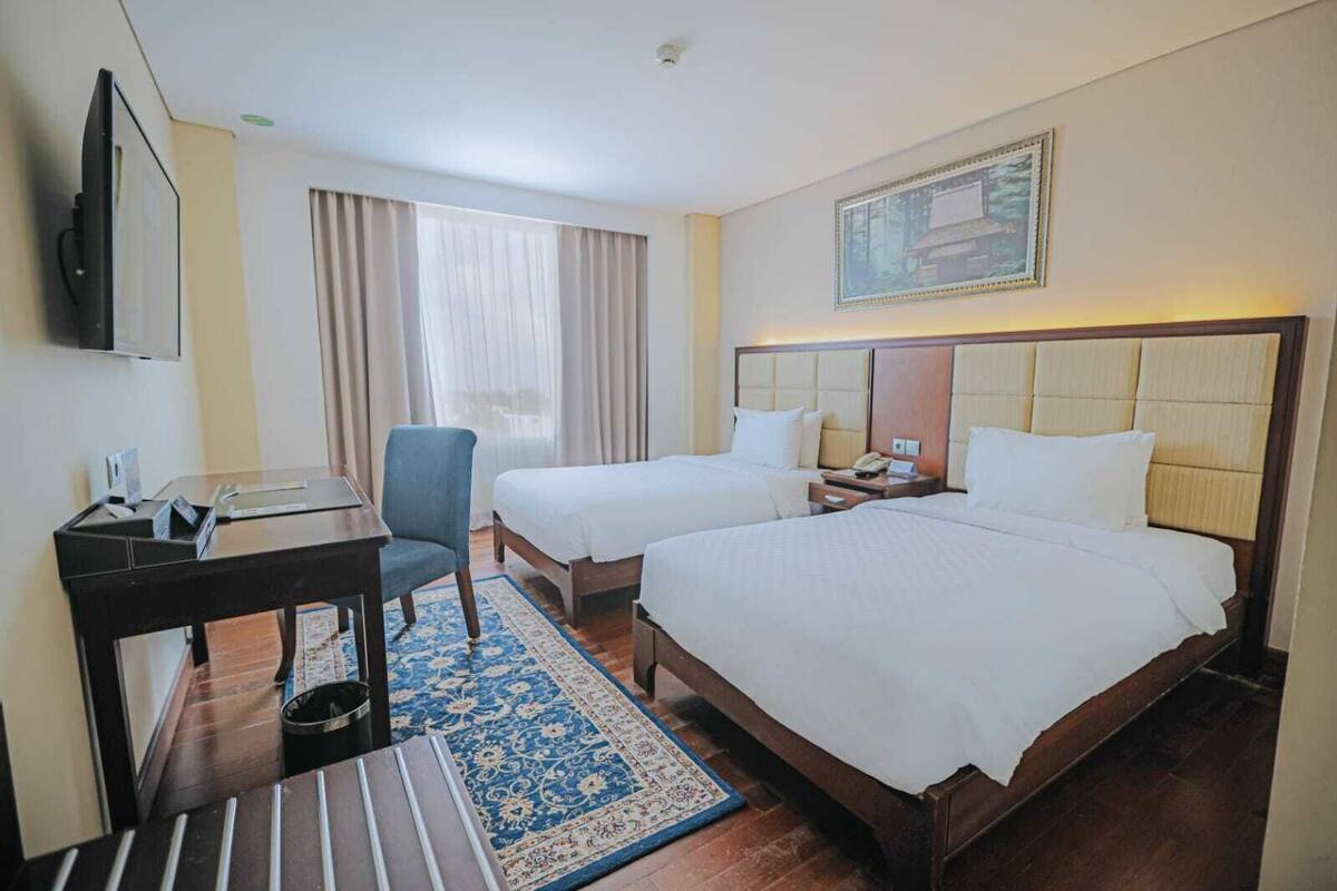 Habitación de hotel con dos camas, un escritorio, una silla, un televisor y un cuadro en la pared.