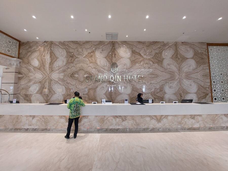 A reception desk at Grand Qin Hotel with a marble wall and a receptionist.