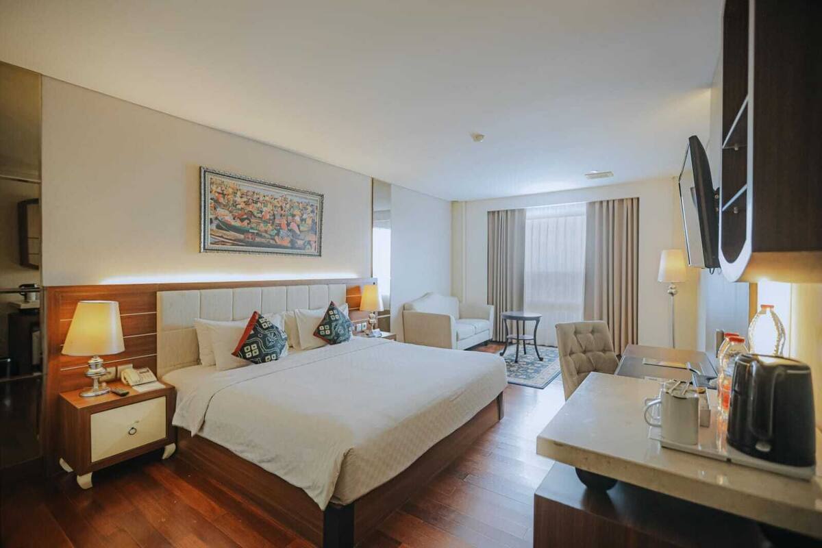 Una habitación de hotel con una cama grande, un escritorio, una silla, un televisor y un cuadro en la pared.