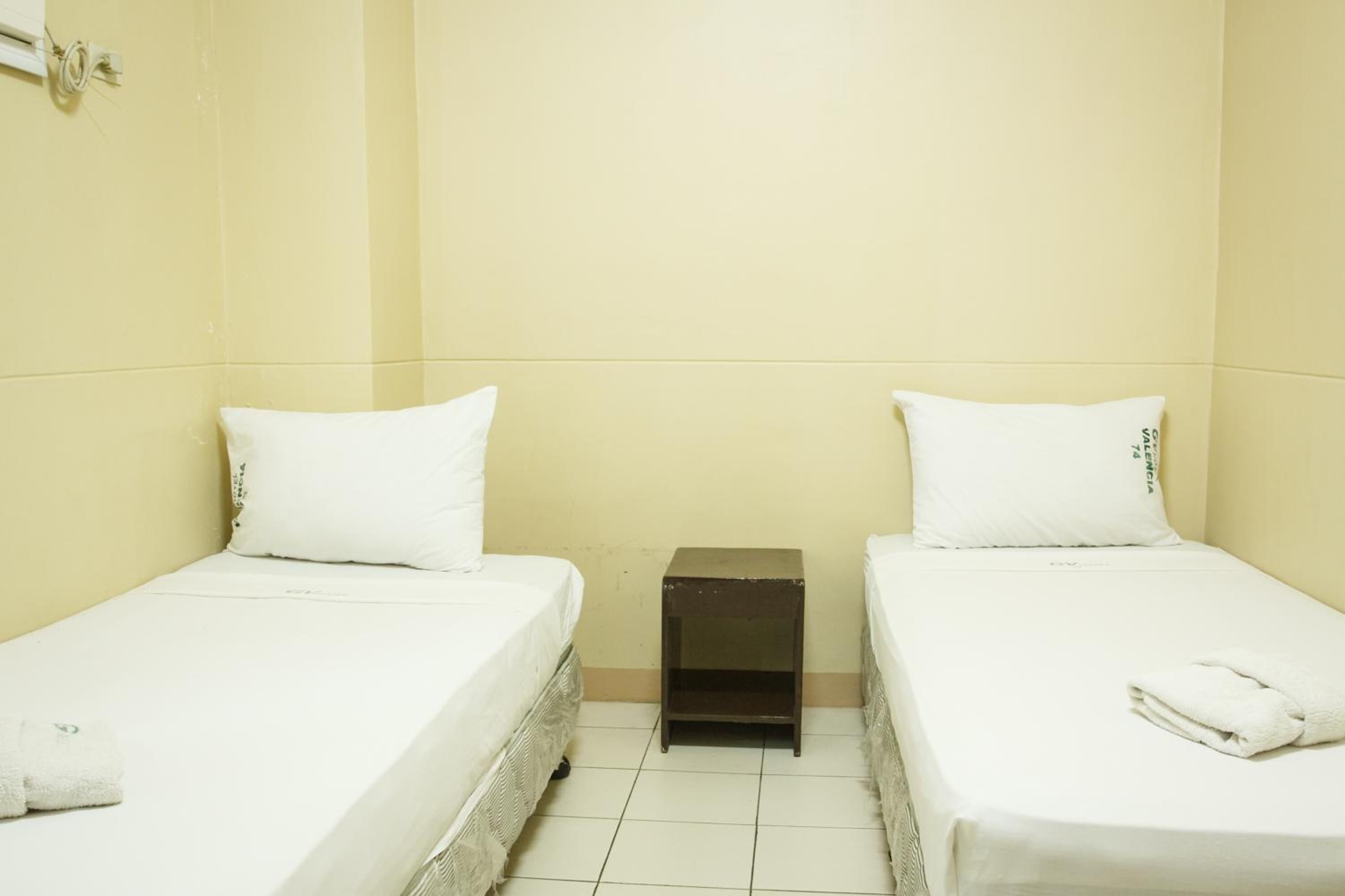 A small, clean room with two single beds, each with a white pillow and a small nightstand.