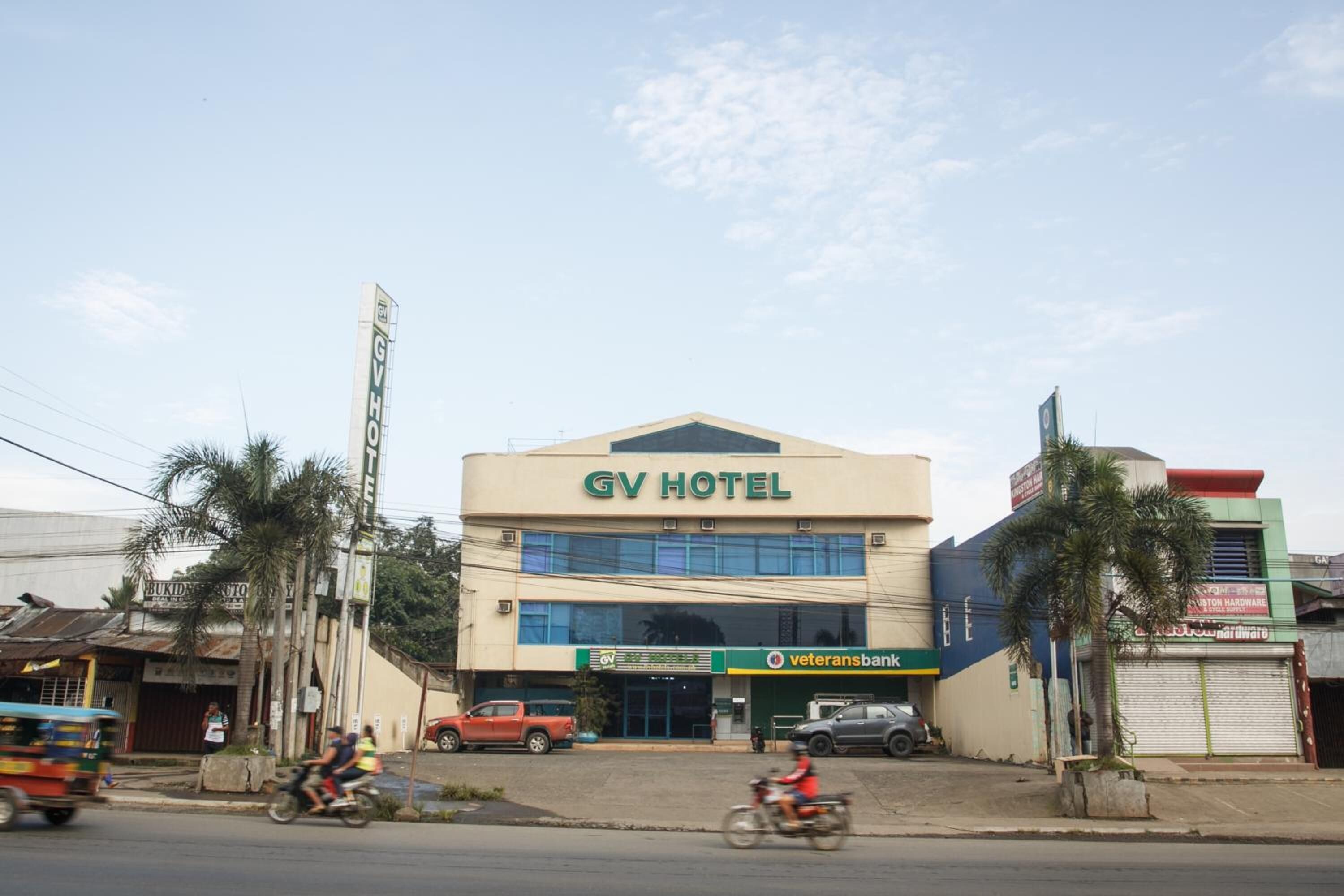 Un hotel con un letrero llamativo, una sucursal bancaria y palmeras en primer plano.