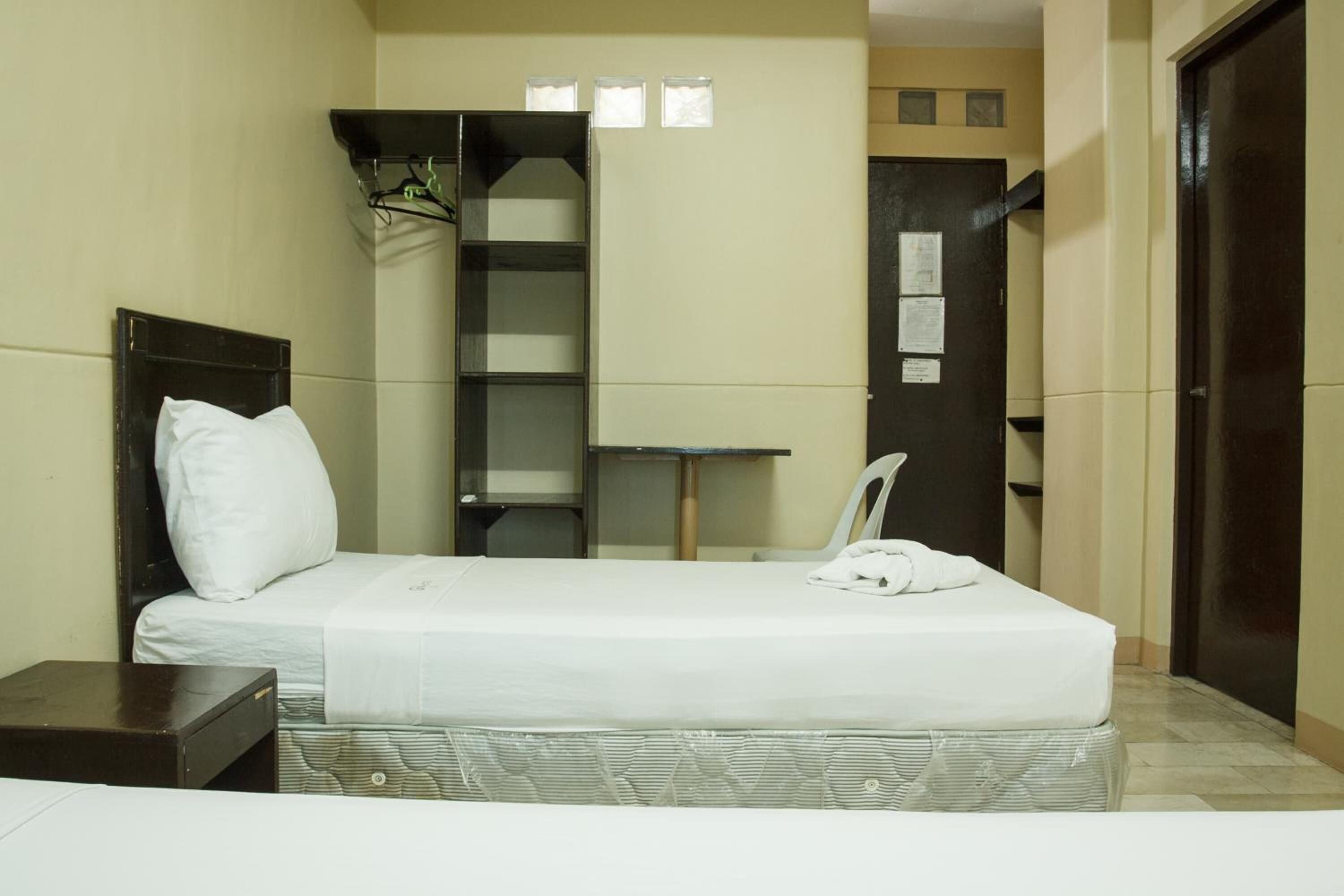 A small, compact hotel room with a single bed, a small table, a chair, and a wardrobe.