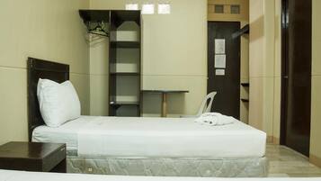 A small, compact hotel room with a single bed, a small table, a chair, and a wardrobe.