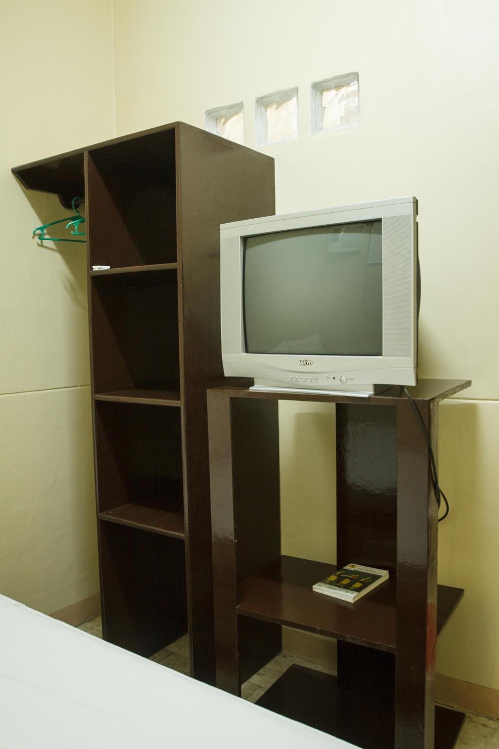 A television on a wooden stand in a room with a white wall and a window.