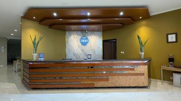 Un mostrador de recepción de hotel con encimera de mármol, paneles de madera y dos plantas en macetas.