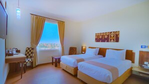 Una habitación de hotel con dos camas, un escritorio, una silla y una ventana con cortinas.