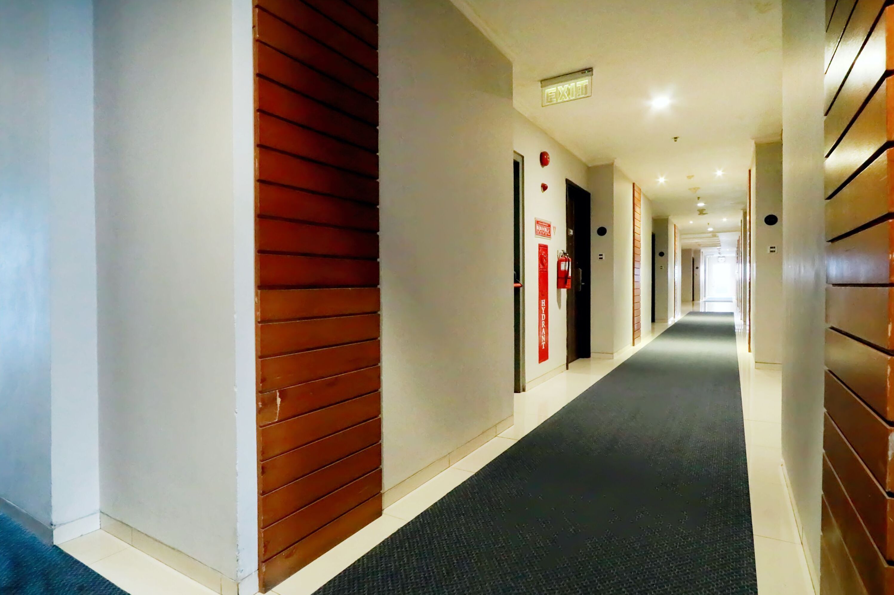 A hotel corridor with a dark carpet, wooden panel walls, and red signage.