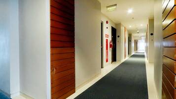 A hotel corridor with a dark carpet, wooden panel walls, and red signage.