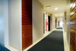 Pasillo de hotel con alfombra oscura, paneles de madera y señalización roja.