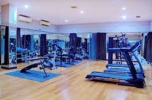 Un gimnasio con equipo de ejercicio, espejos y suelo de madera.