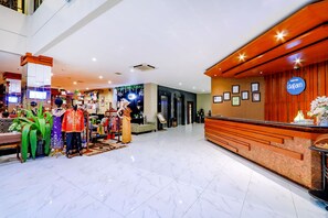 Eine Hotelhalle mit Empfangstresen, einer Sitzecke und einer Präsentation farbenfroher traditioneller Kleidung.