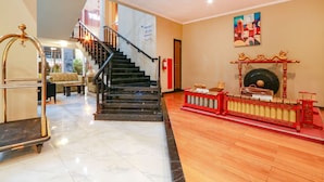 Un vestíbulo de hotel con una escalera, un adorno rojo y dorado, y un cuadro en la pared.