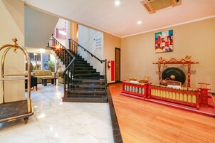 Un vestíbulo de hotel con una escalera, un adorno rojo y dorado, y un cuadro en la pared.