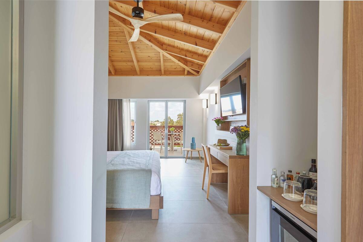 Een moderne slaapkamer met een houten plafond, een bed, een bureau en uitzicht op de omgeving.