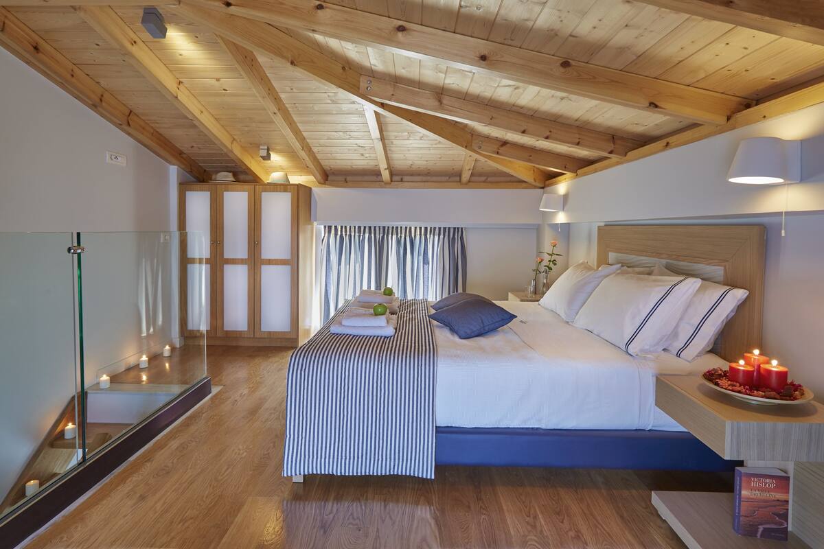 Een slaapkamer met een houten plafond, een bed met witte lakens, een nachtkastje met kaarsen en een spiegel.