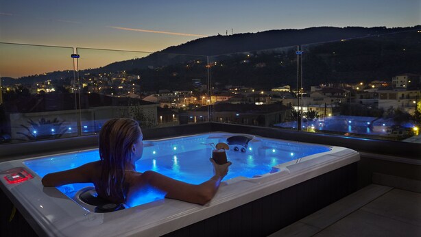 A person relaxing in a hot tub with a city view at dusk. - Mystery Skiathos Luxury Residence  (Skiathos)