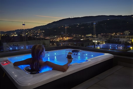 A person relaxing in a hot tub with a city view at dusk.