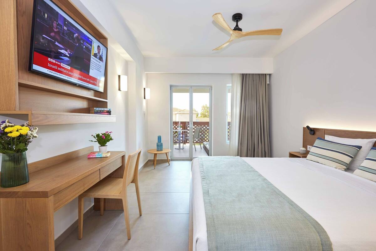 Hotelkamer met bed, bureau, televisie, plafondventilator en uitzicht.
