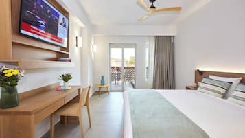 A hotel room with a bed, desk, TV, ceiling fan, and a view of the outside.