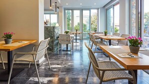 A modern dining area with wicker chairs, wooden tables, and large windows offering a view of the outdoors. - Mystery Skiathos Luxury Residence  (Skiathos)