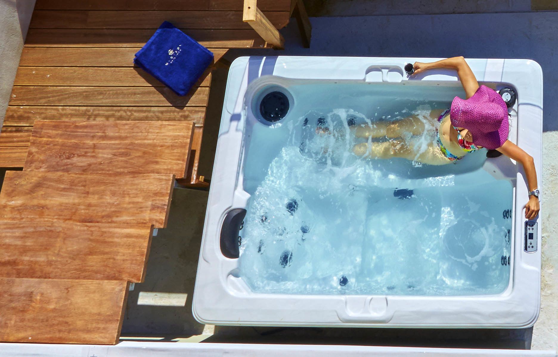 Un bain à remous avec une personne portant un maillot de bain rose, une terrasse en bois et une serviette bleue.