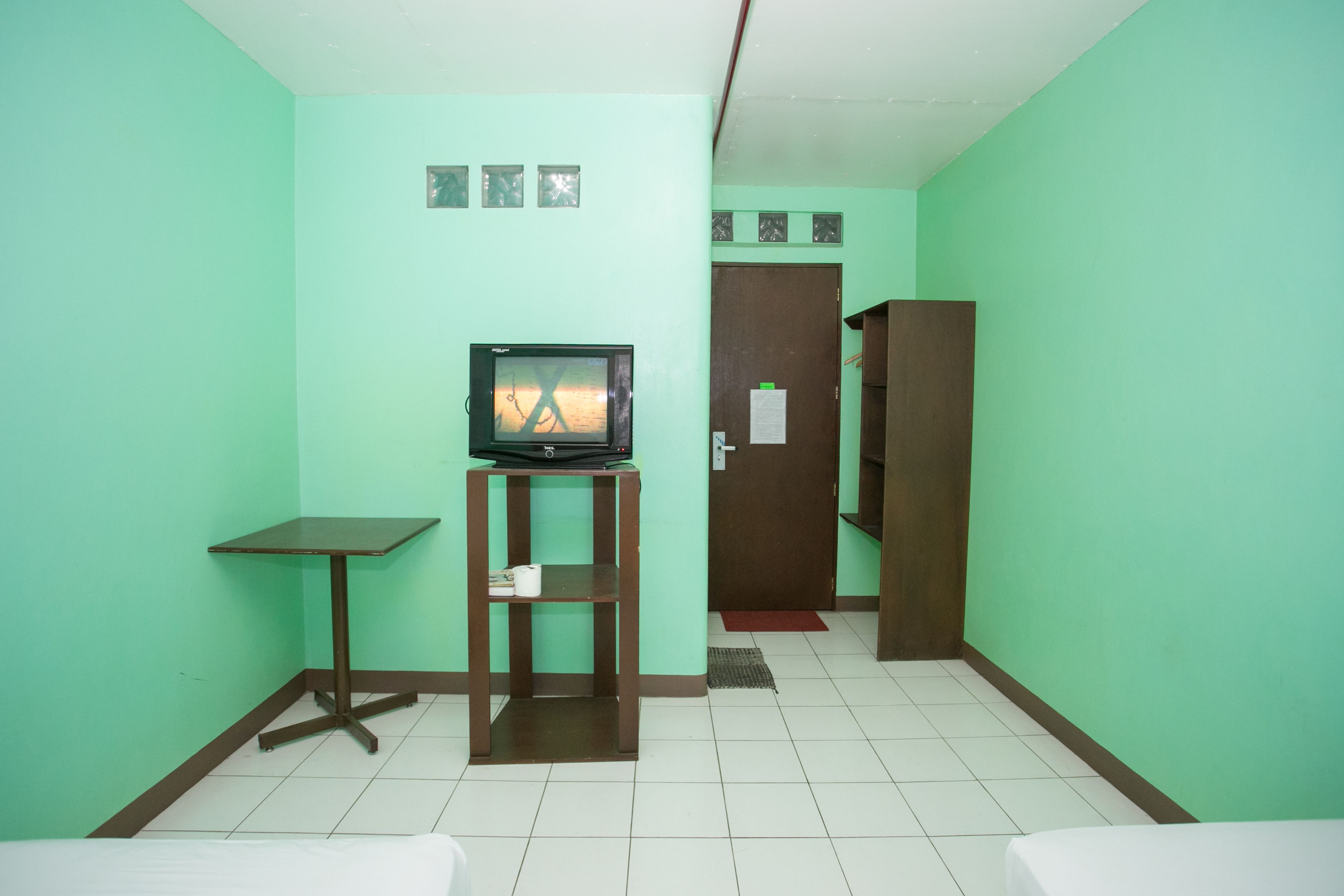 A small room with teal walls, a bed, a TV on a stand, a door, and a small table.