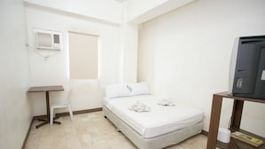 Una habitación pequeña y limpia con cama, escritorio, silla y televisor.