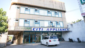 Un edificio de dos pisos con un letrero que dice 'CITI APPLIANCE' en la planta baja. Se observan unidades de aire acondicionado en el exterior, y un coche blanco estacionado al frente.