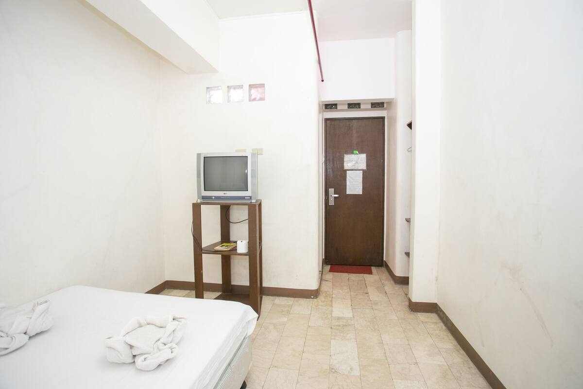 A hotel room with a bed, a TV on a small stand, and a door with a red mat.