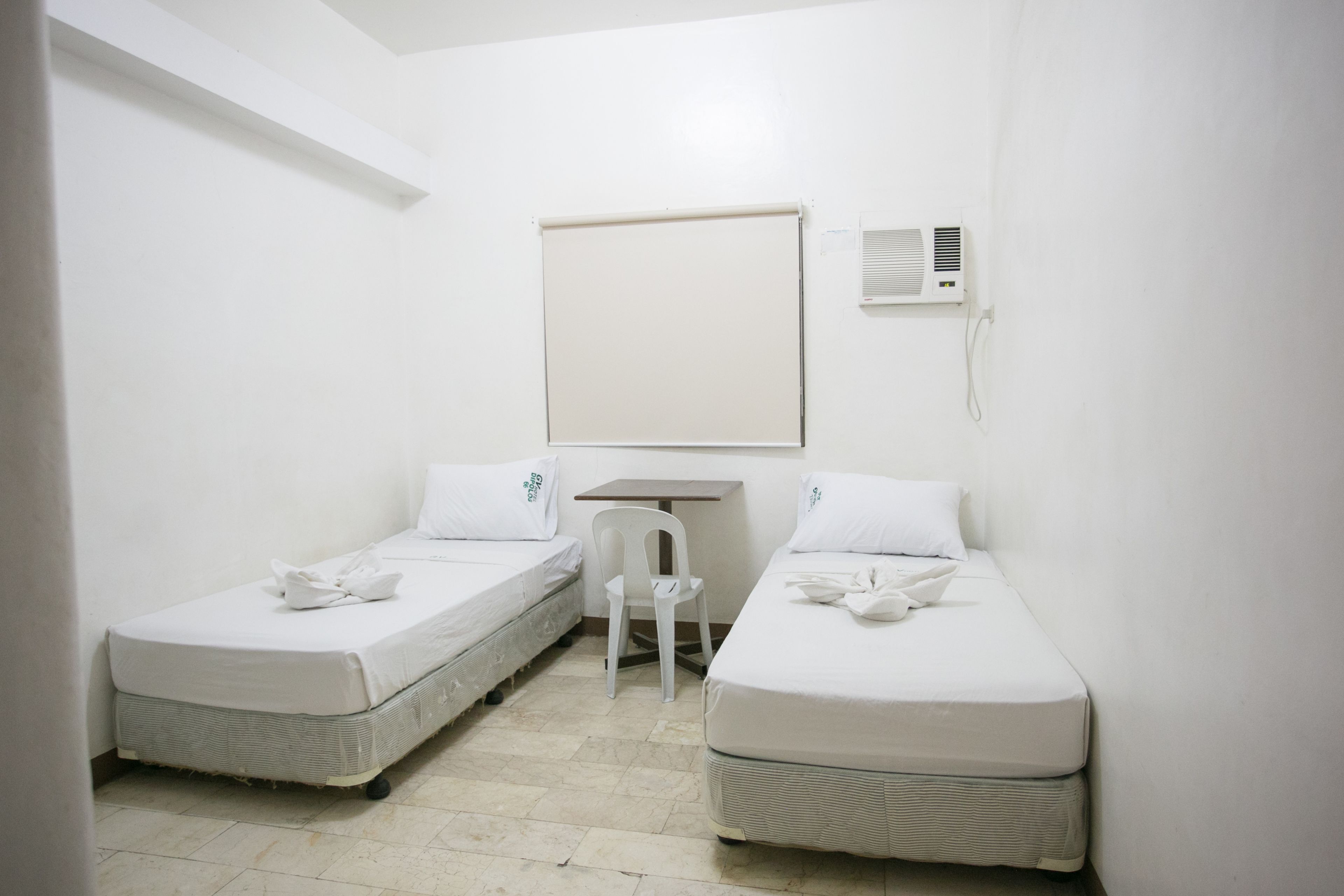 Una habitación pequeña y limpia con dos camas individuales, un escritorio y una silla.