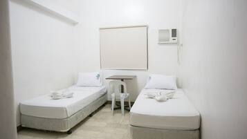 Una habitación pequeña y limpia con dos camas individuales, un escritorio y una silla.