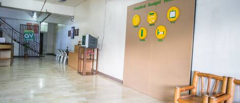 A hotel lobby with a sign indicating practical budget rooms, a reception desk, and a staircase.
