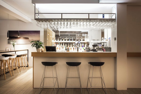 Un espace bar moderne avec un comptoir en bois, des tabourets de bar et une variété de bouteilles et de verres.